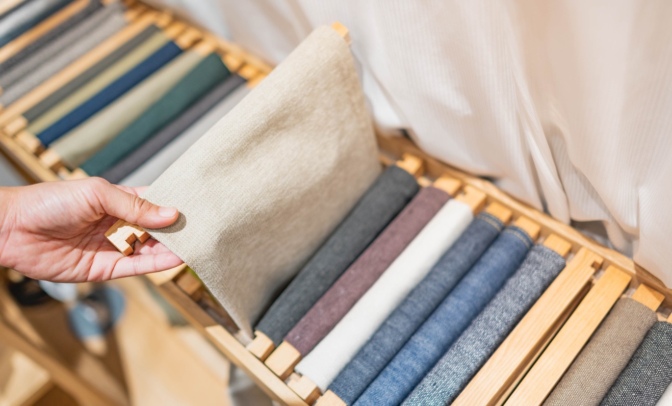 The girl's hand is choosing the roll of fabric and textile. The roll of fabric are the earth-tone cone.